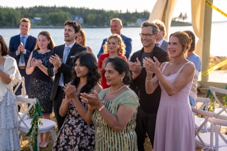 A crowd of guests, male and female, at a wedding ceremony, with the sea behind them
