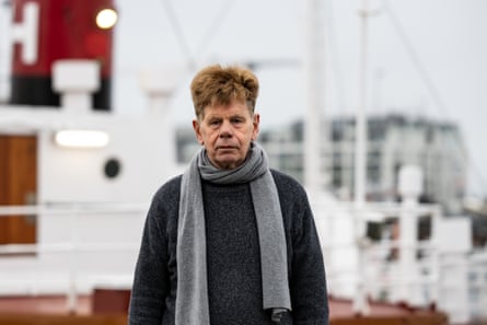 An older man with a crumpled face seen in front of ships