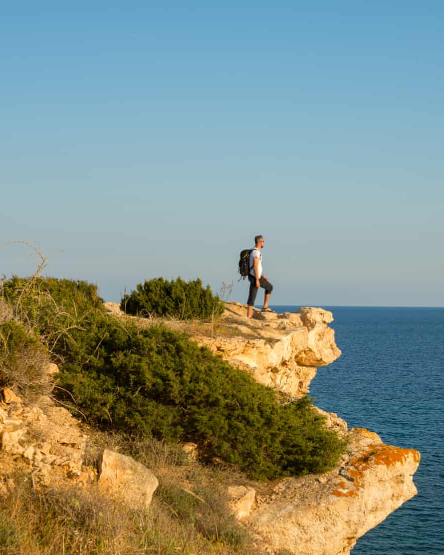 Hiker with backpack standing on the rocky cliff on the shore of Cape Greco.