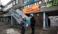Patrick Barry, 77, stands with a campaigner in front of a block of low-rise flats; there are banners on the steps and first-floor concrete walkways with messages including Retrofit Don't Demolish and Housing Rebellion