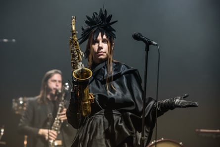 A woman dressed in black with headdress on stage with a saxophone in hand