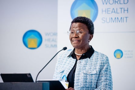 An African woman stands at a podium with a microphone. Behind her a sign says ‘World Health Summit’