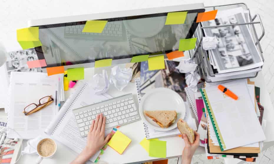 Office worker at messy office desk eating a sandwich