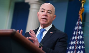 A man in a suit and tie speaks at a lectern with an American flag in the background