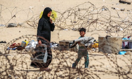 A woman and boy walk with belongings past barbed-wire fences as they flee from Rafah in southern Gaza on Saturday.