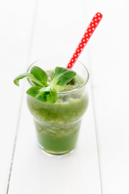 Glass full of lamb’s lettuce smoothie with spoon on white wooden table