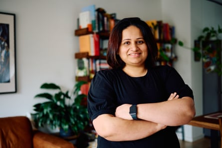 A woman standing in her apartment with her arms crossed, smiling gently.