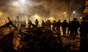 Riot police walk past burnt chairs and tables, during a protest of gilets jaunes (yellow vests).