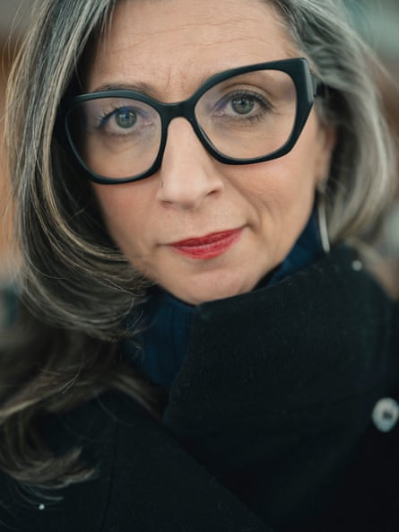 A close-up of Albanese. She is wearing a dark top, dark-rimmed glasses and red lipstick
