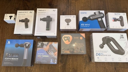 Nine massage guns in their boxes on a wooden floor