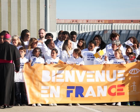 People stand behind a banner reading in French "welcome in France" as they wait for the arrival of Pope Leo XIV outside Orly airport, in the outskirts of Paris.