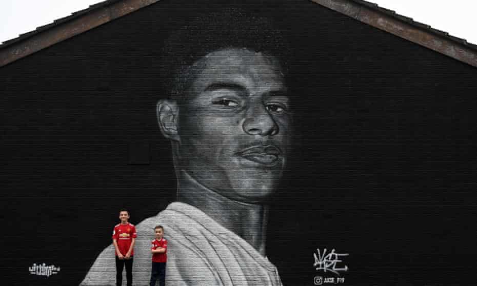 Children in Manchester United shirts pose against a mural of Marcus Rashford in Withington, Manchester by graffiti artist Akse P19