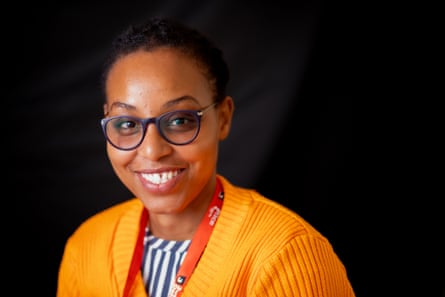 A woman wearing glasses and a bright orange jumper smiles at the camera