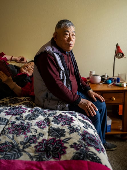Man fully clothed sits on neatly made bed.
