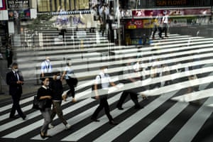 Commuters are reflected in a bus window as they cross the street in Tokyo