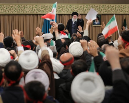 Khamenei in a room of supporters, some of whom are waving Iranian flags