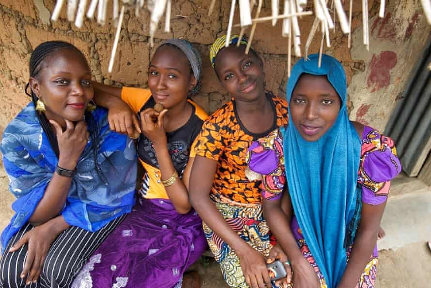 An older woman with three girls in traditional African print dresses outside a hut