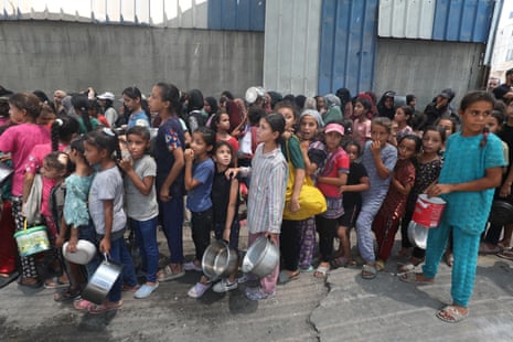 Palestinians, including children, who are struggling to access food due to Israel’s blockade and ongoing attacks on the Gaza Strip, wait in line to receive hot meals distributed by the charity organisation at the Nuseirat refugee camp in Deir al-Balah, Gaza, on 18 August 2025.