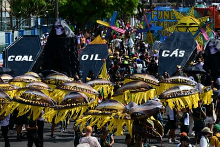 Parade full of people with yellow umbrella costumes and three coffins, labeled Coal, Oil and Gas.