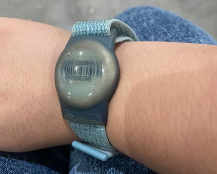A wrist-worn device resembling a digital watch but showing a barcode rather than the time