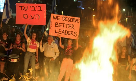 People standing near a fire with banners, one of which says: ‘We deserve better leaders.’