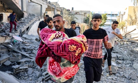 A man carries a victim of an Israeli airstrike, wrapped in a blanket, through rubble in Rafah in the southern Gaza Strip.