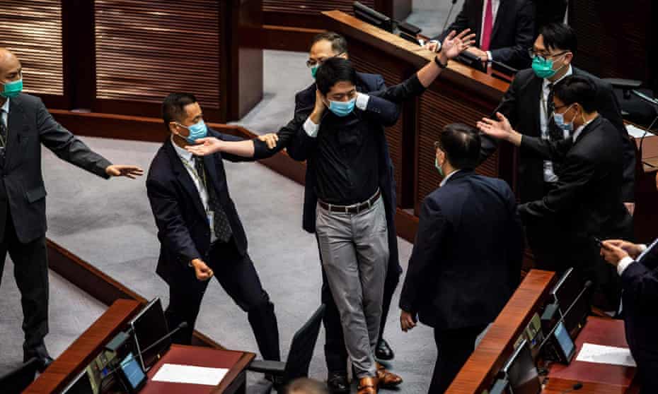 Ted Hui (C) is removed by security guards after throwing a jar containing a foul-smelling liquid onto the floor during a debate on a law that bans insulting China’s national anthem