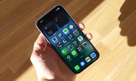 The iPhone 15 showing the home screen held in a hand.