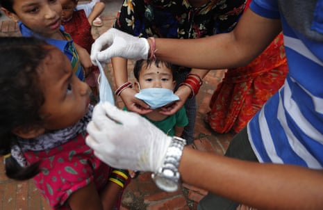 A volunteer provides free face masks to children who have come to see Machindranath chariot festival, which was postponed at the last minute as a precaution against the spread of coronavirus in Lalitpur, Nepal, on Saturday, 25 July, 2020.