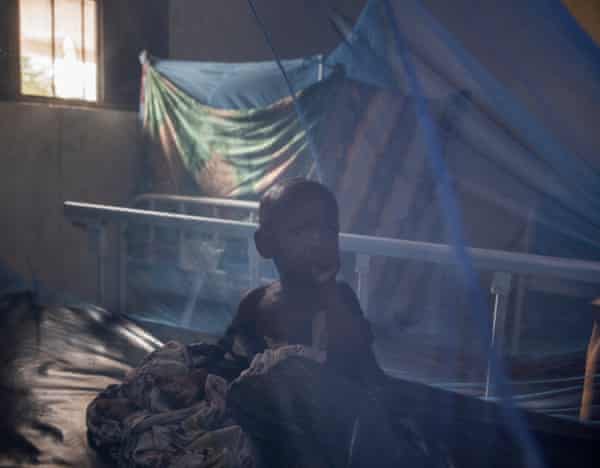 A baby seen through a mosquito net in a dimly lit hospital ward