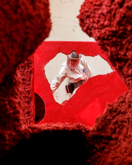 A person in a hazmat suit working on a big, red sculpture.