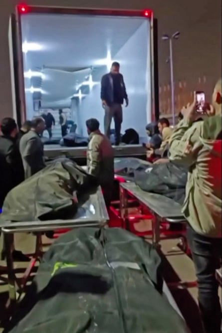 People stand beside bodybags on stretchers