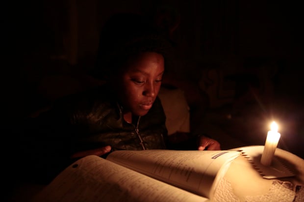 Rubimbo Makombe reads by candlelight during a power outage in Harare on July 28, 2022.
