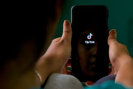 Uma mulher segura um smartphone com o logotipo do TikTok em um fundo preto.