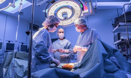 Doctors wearing surgical masks and gowns performing an operation on patient in hospital operating theatre