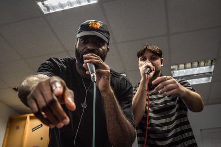 They gesticulate towards the camera, holding mics in their hands