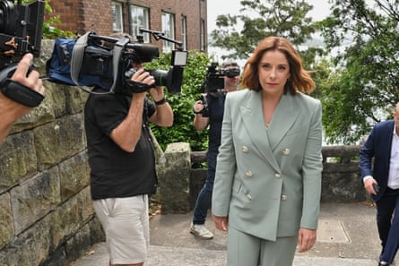 Anika Wells in a double-breasted suit walks passed camera operators