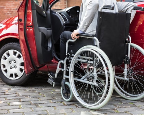 Photo of a young man sitting in a wheelchar as he prepares to get into a red car