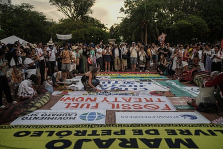 Dozens of people stand around a selection of banners on the ground, one of which reads: ‘Fossil fuel treaty now’