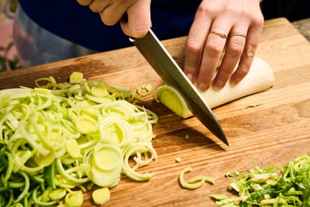 The cook using a large knife to chop up leaks on a wooden chopping board