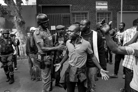 Monochrome picture of a police officer putting his hand on the arm of a man as he makes a gesture of anger.
