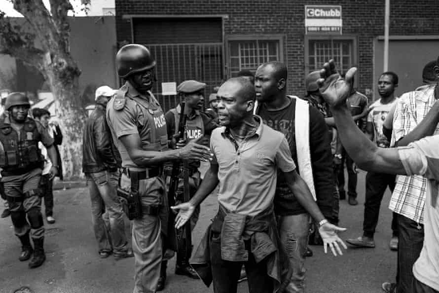 Monochrome image of a police officer putting his hand on a man's arm while gesturing in anger.