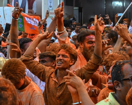 Men coated in orange powder raise their hands and smile