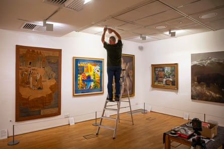 Man on a stepladder doing something on the ceiling in a room of artworks