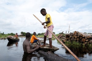 Ikuejamoye talks with local people as he pulls his logs through the river