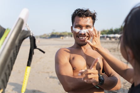 A womn applying sunscreen to a man’s face at the beach