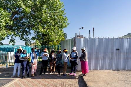 Women stand in a line outside fence of a factory.