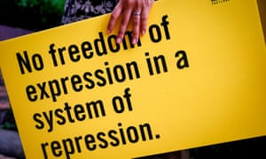 A woman holds an Amnesty placard saying 'No freedom of expression in a system of repression'