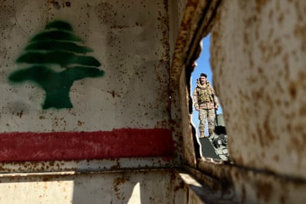 A Lebanese soldier stands outdoors, photographed through a damaged military vehicle