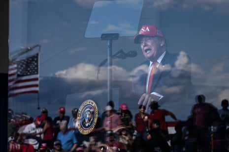 Reflection of Donald Trump speaking at a rally podium, with a crowd below